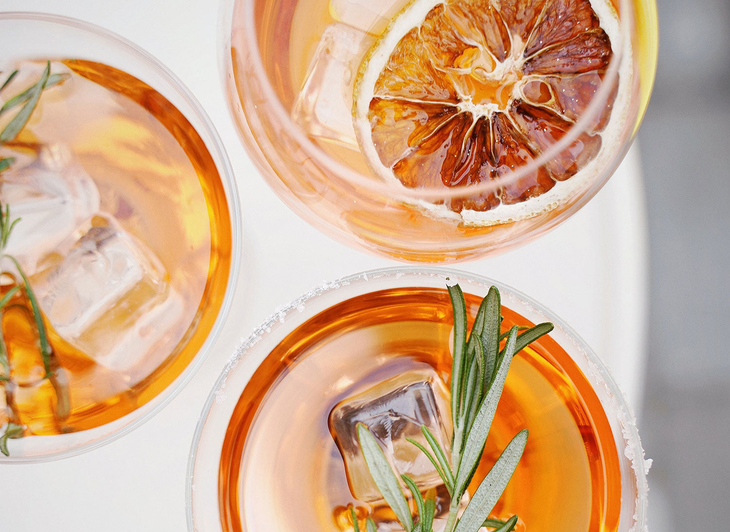 Sliced orange fruit, rosemary, and ice cubes in clear drinking glasses. Image by Olena Bohovyk