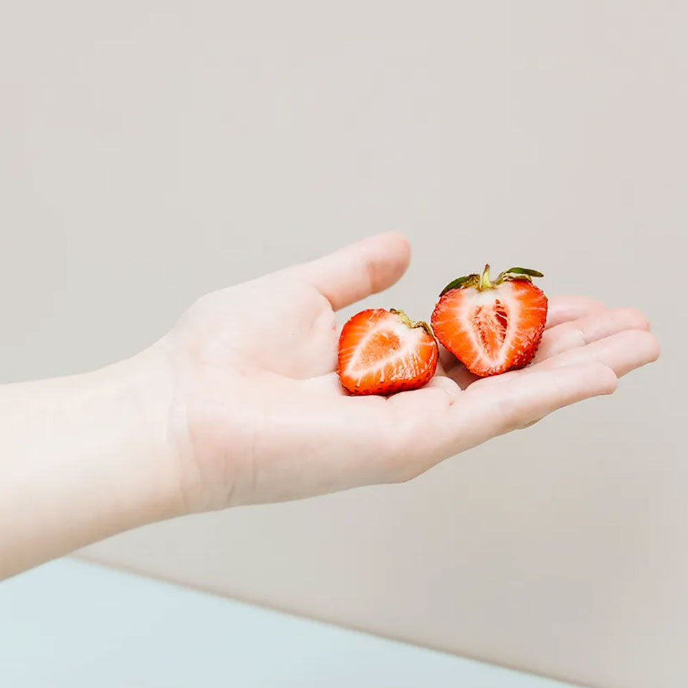 White hand holding sliced strawberry against a tan background.