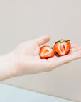 White hand holding sliced strawberry against a tan background.